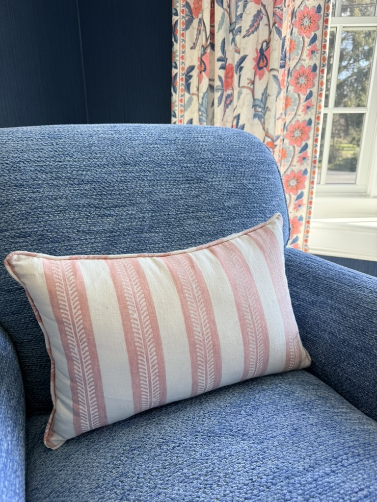 Blue upholstered chair with pink striped pillow and floral curtains